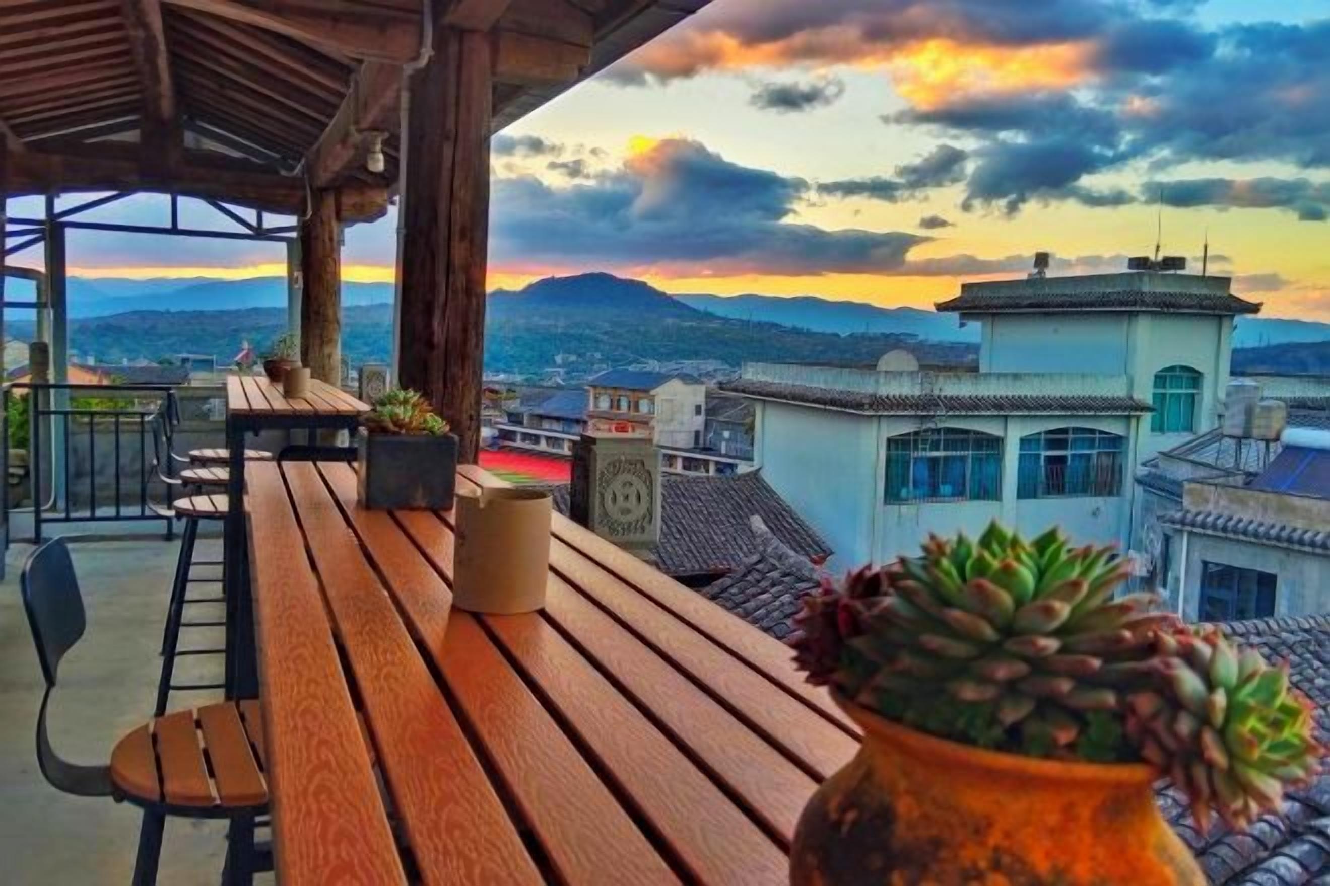 Terraza de madera con una planta en maceta, con vistas a un paisaje urbano que incluye edificios y montañas.