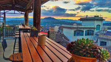 Terraza de madera con una planta en maceta, con vistas a un paisaje urbano que incluye edificios y montañas.