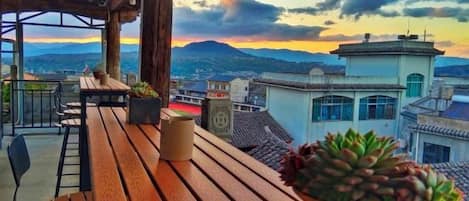 A wooden deck with a potted plant, overlooking a cityscape with buildings and mountains.
