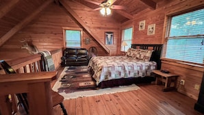 A cozy attic bedroom with a wooden ceiling, a bed with patterned bedding, a leather chair, and a small table. - Labor Day at Pike's Peak - Wifi and Hot Tub! - Callaway Gardens (Warm Springs)