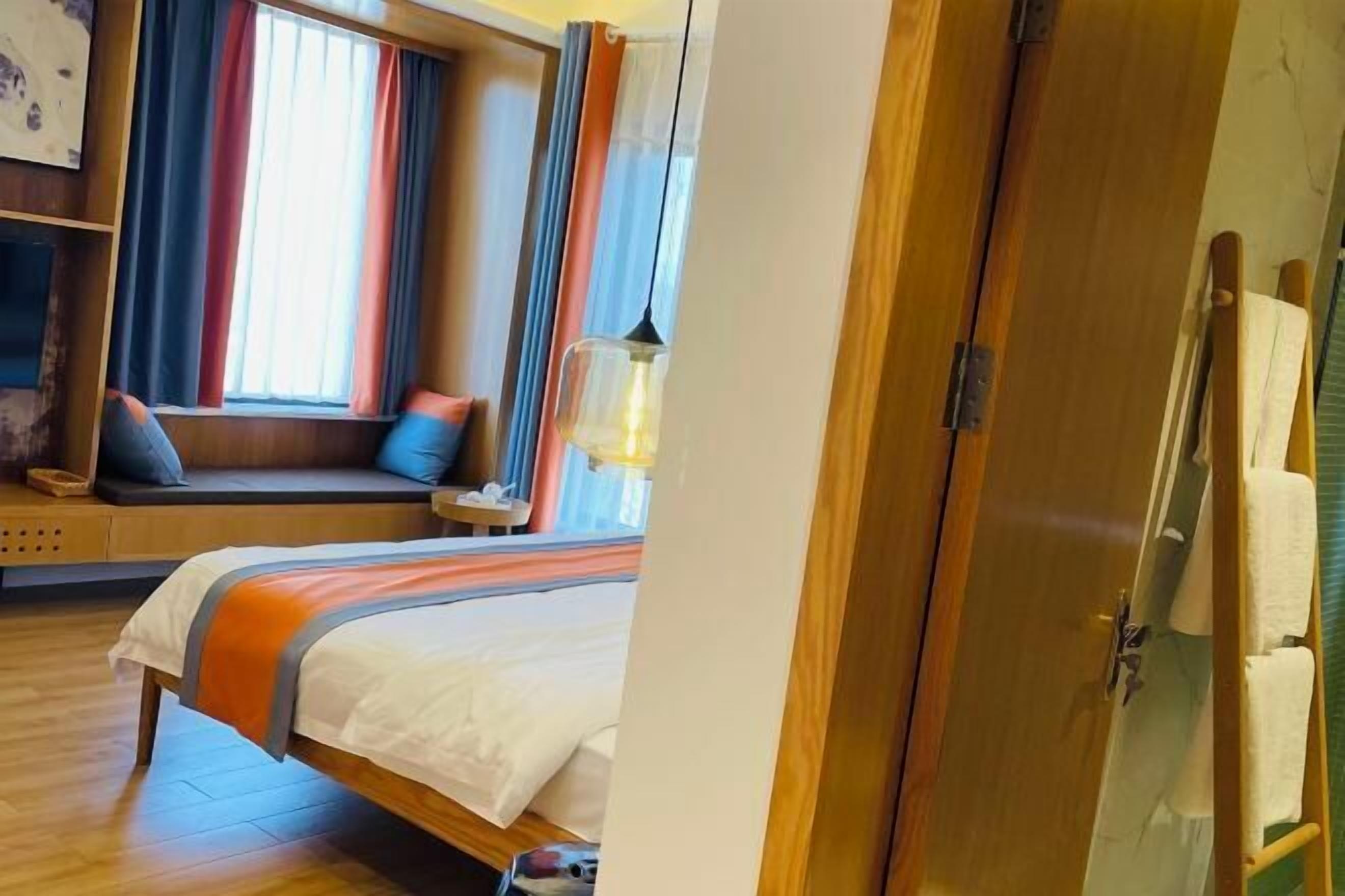 A hotel room with a bed, a window with curtains, a bedside table, and a lamp.