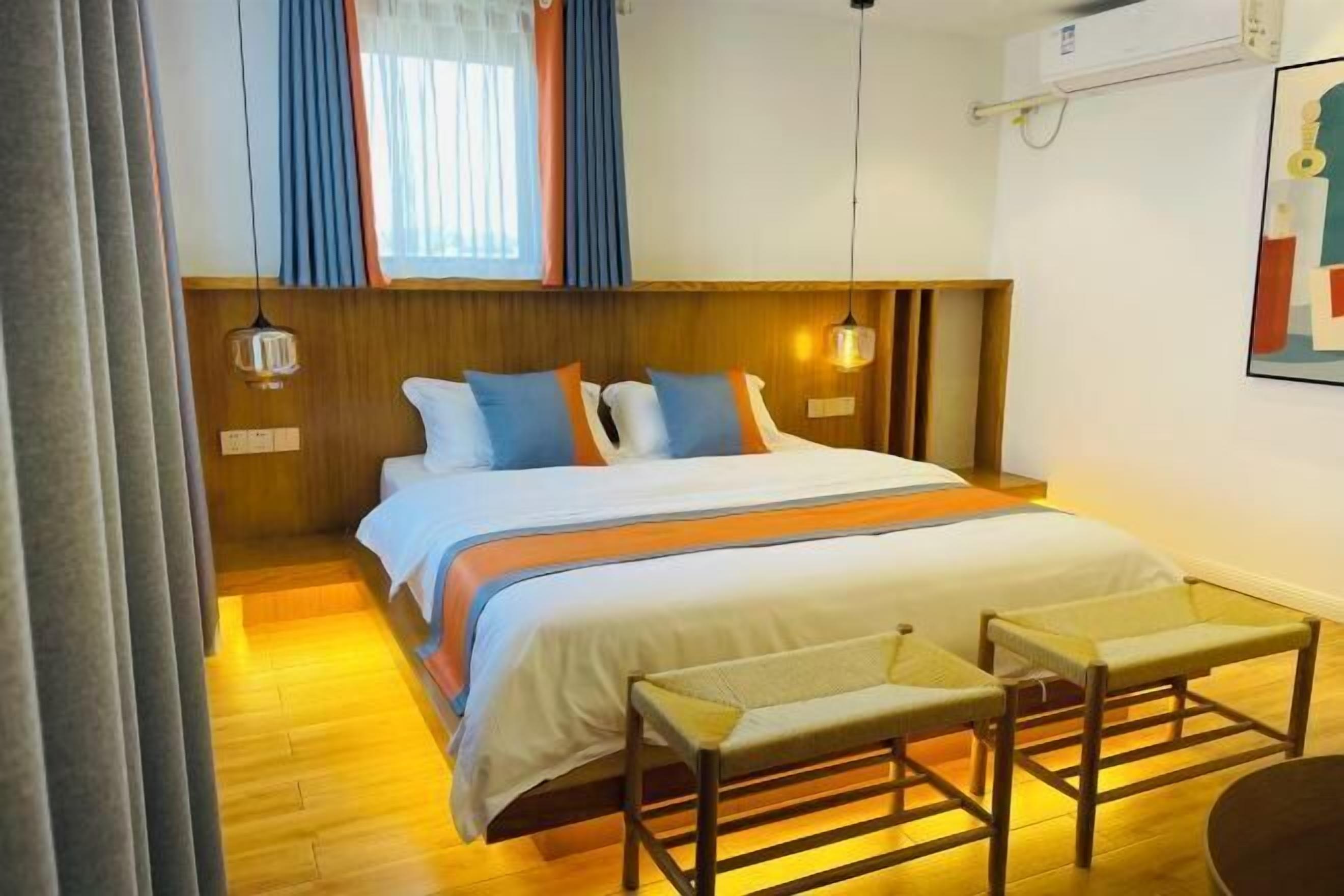 A hotel room with a wooden headboard, a bed with white and orange bedding, a bench, and a small table.
