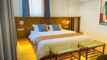 A hotel room with a wooden headboard, a bed with white and orange bedding, a bench, and a small table.