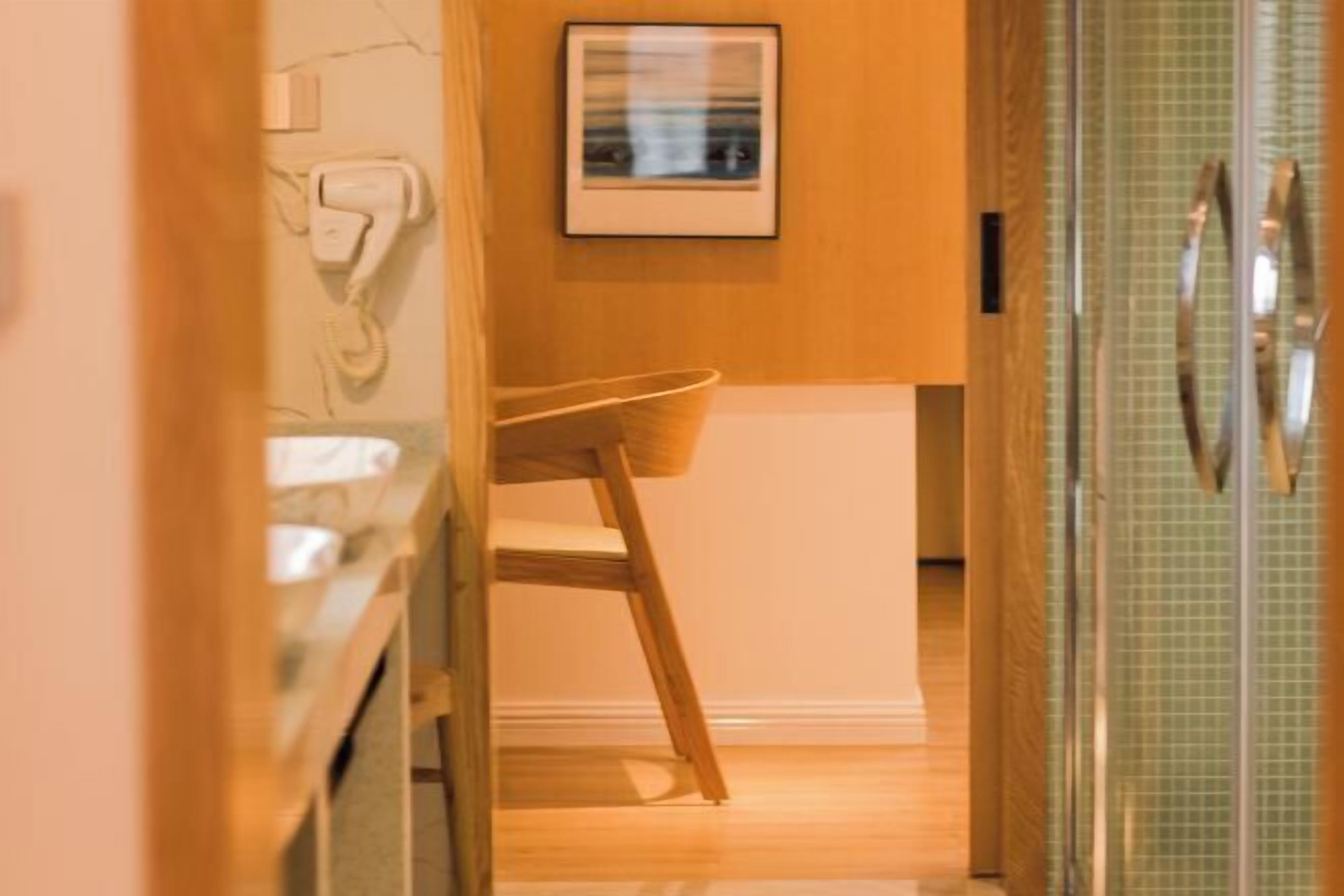 A hallway with a wooden chair, a framed picture on the wall, and a glass shower door.