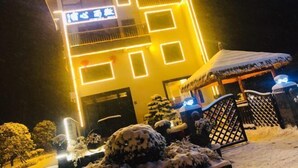 Un edifici de diverses plantes amb patrons geomètrics il·luminats a la façana, una entrada amb reixa i jardineria coberta de neu.
