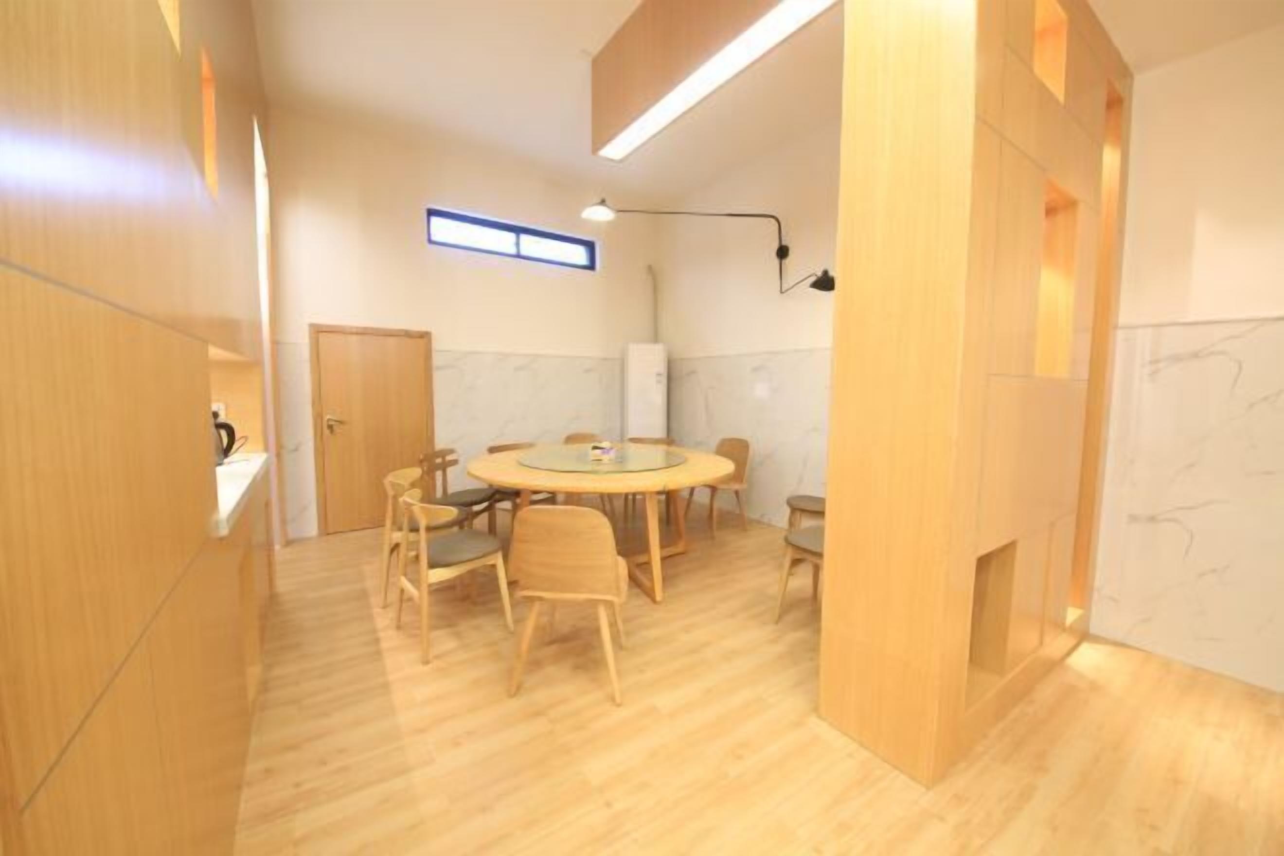 Une pièce moderne avec une table ronde, des chaises en bois, un réfrigérateur et une fenêtre avec des stores.