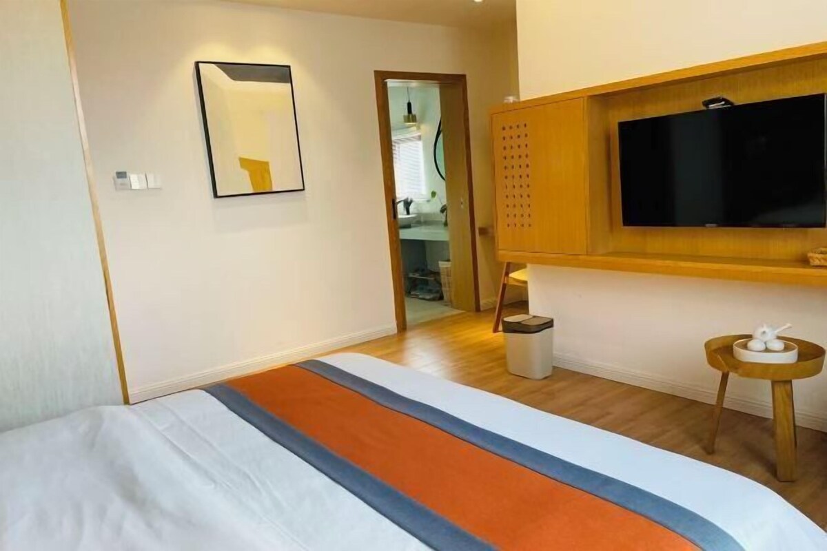 A hotel room with a bed, a television, a small table, and a bathroom visible through an open door.