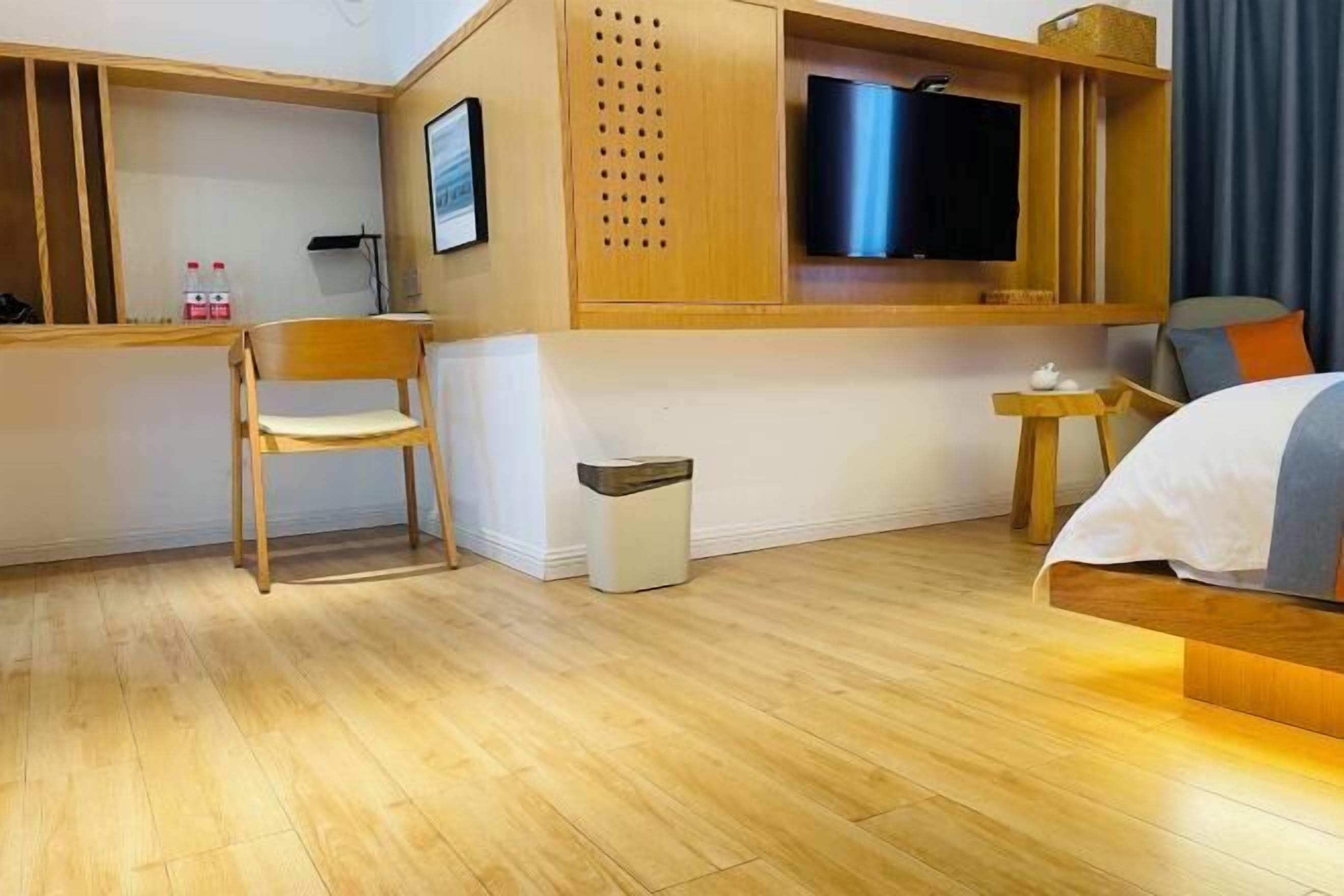 Une chambre d’hôtel avec un plancher en bois, un lit avec une literie blanche et bleue, un téléviseur fixé sur un panneau en bois, une petite table en bois avec une théière et une chaise.