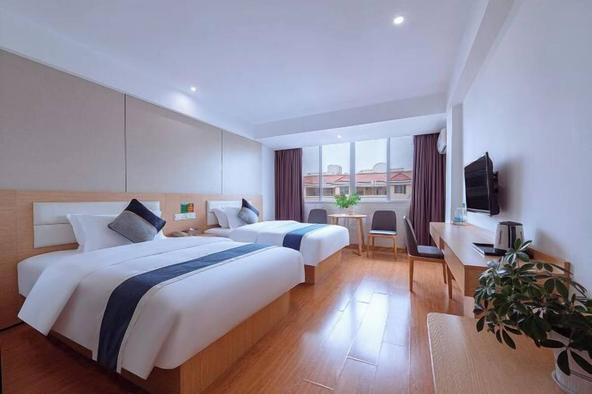 A hotel room with two beds, a desk, a chair, a television, and a window with curtains.
