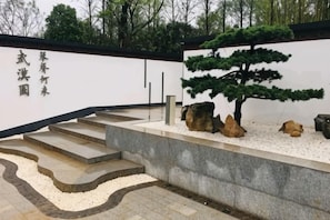 A stone staircase leading to a white wall with Japanese characters, a bonsai tree, and rocks.