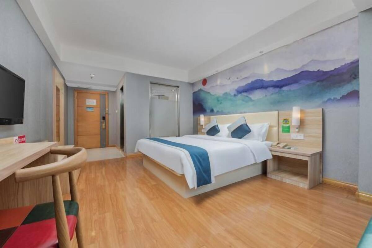 A hotel room with a bed, bedside table, chair, and a painting on the wall.