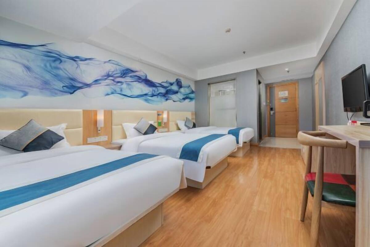 A hotel room with three beds, a wooden floor, a large abstract painting, a television, and a desk with a chair.