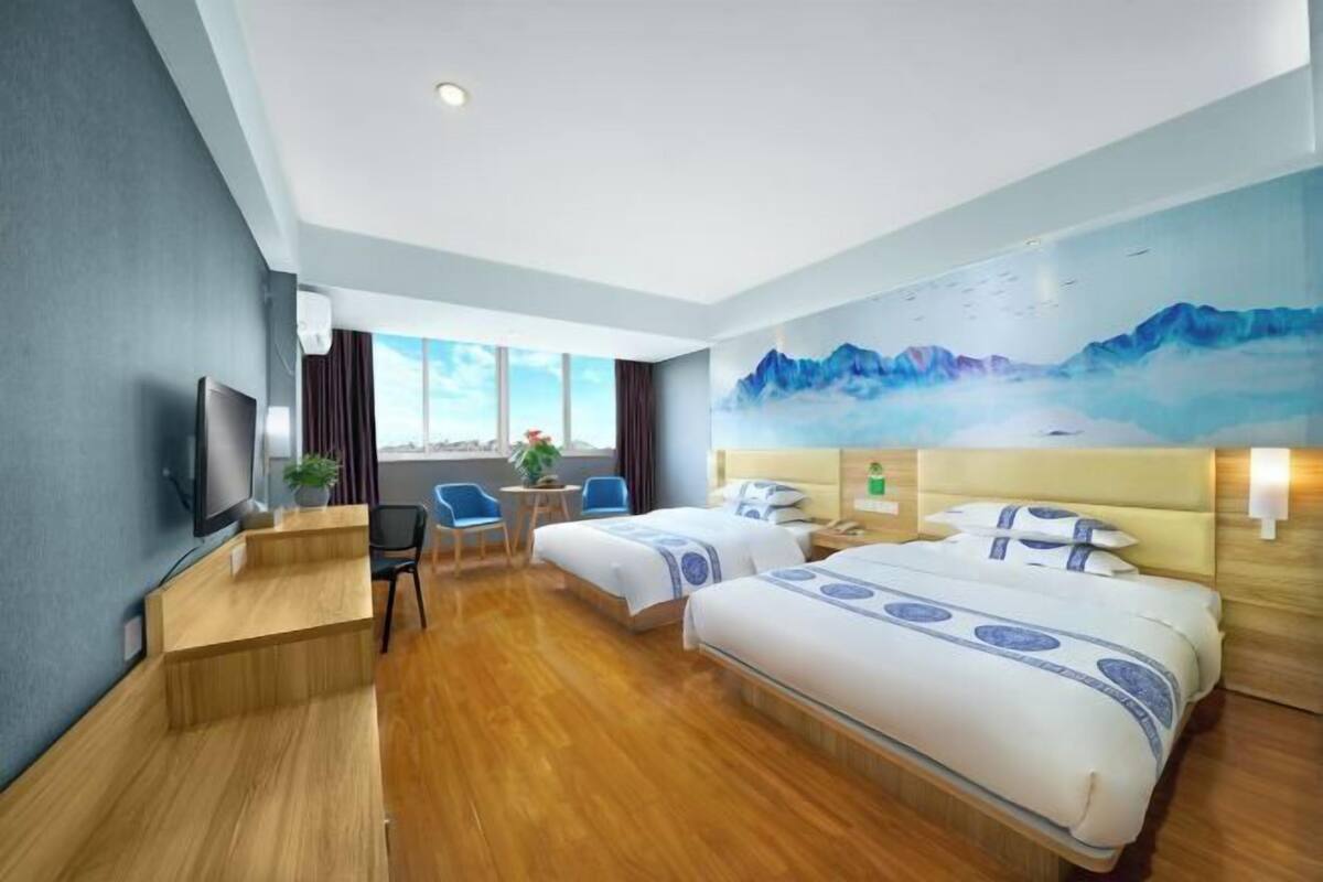 A hotel room with two beds, a desk, a chair, a TV, and a painting on the wall.