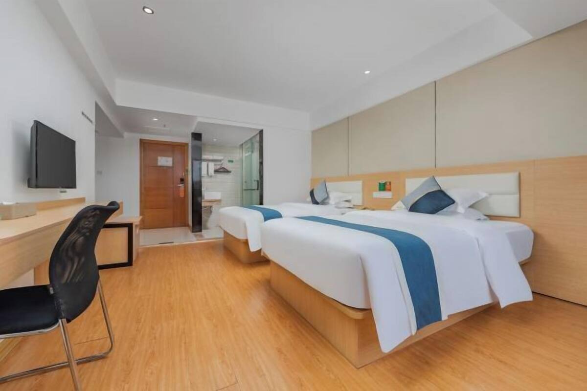 A hotel room with two beds, a desk, a chair, and a television.