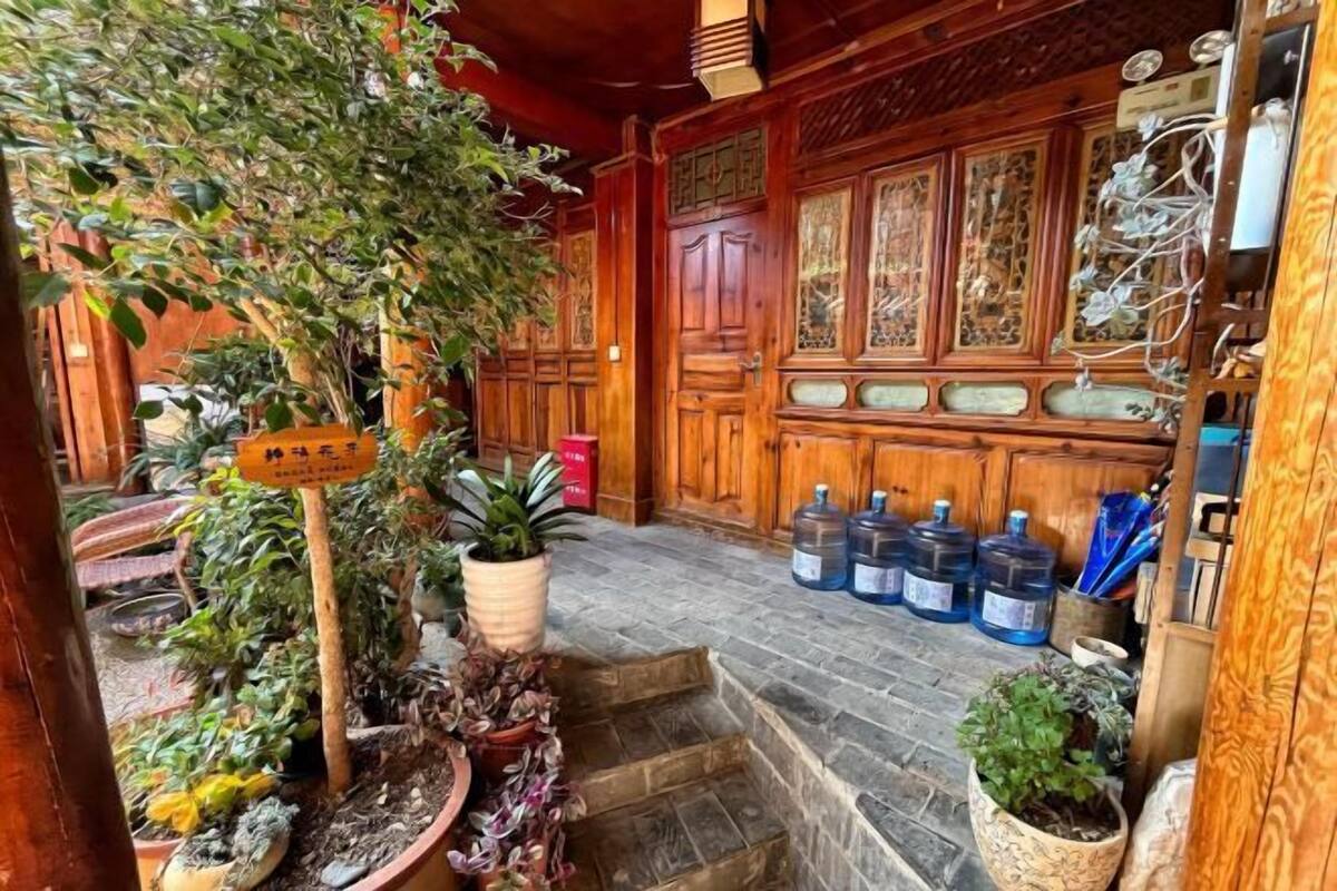 A traditional wooden building with a staircase leading to a door, surrounded by potted plants and large water containers.