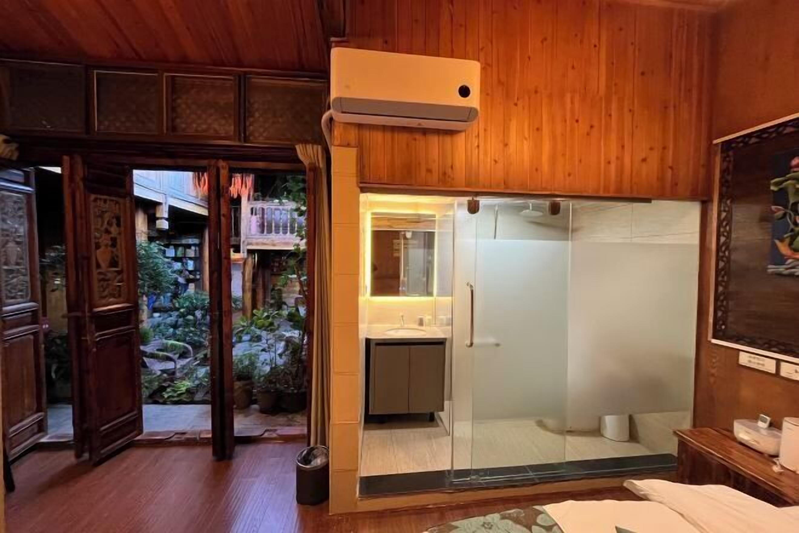 Un interno in legno con cabina doccia in vetro, lavandino a vista e una porta che dà su un'area esterna con piante.
