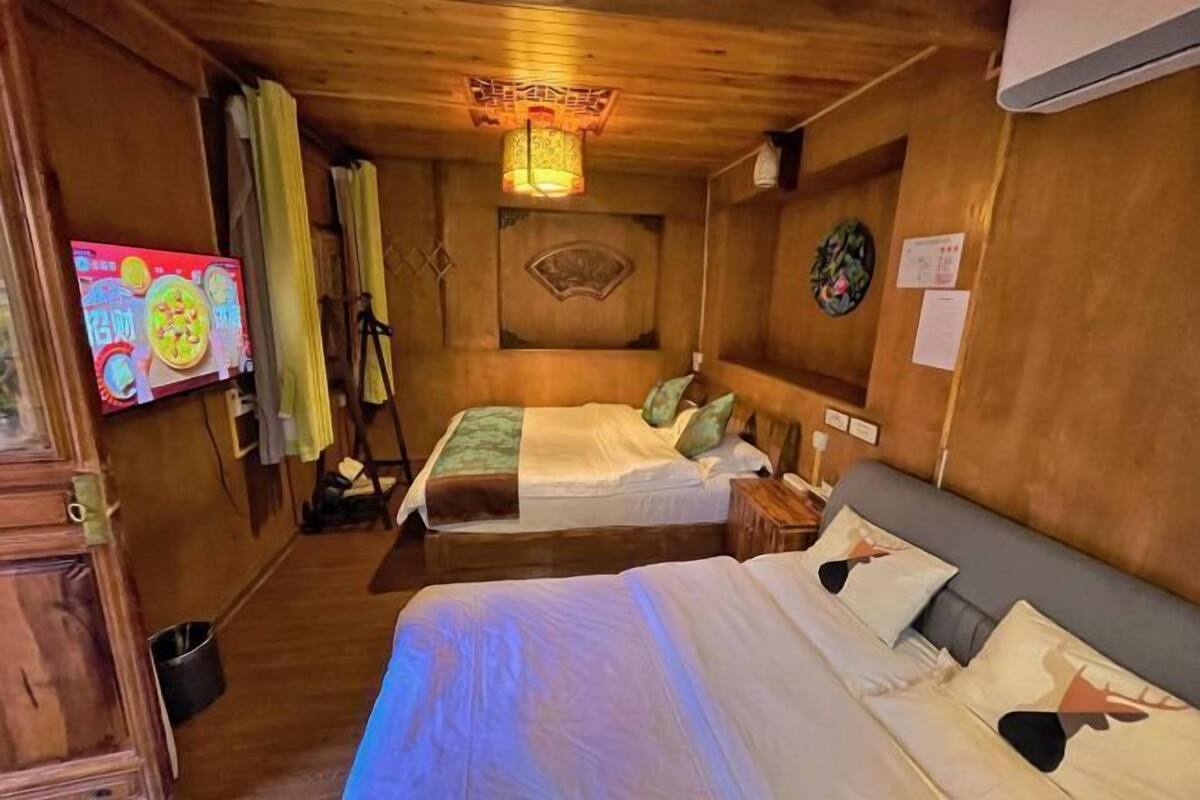 A room with two beds, a television, a wooden ceiling, and a wall with a decorative panel.