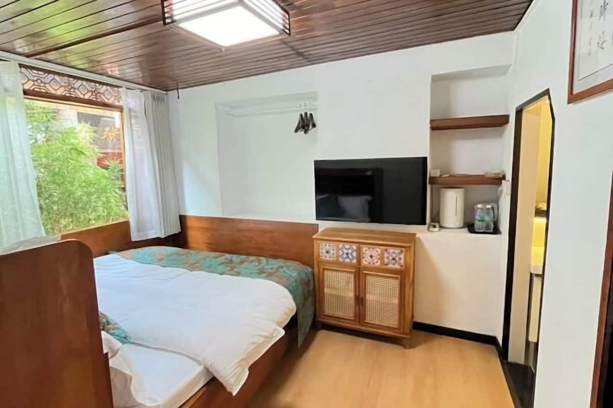 A bedroom with a wooden bed, a TV, a cabinet, and a window with curtains.