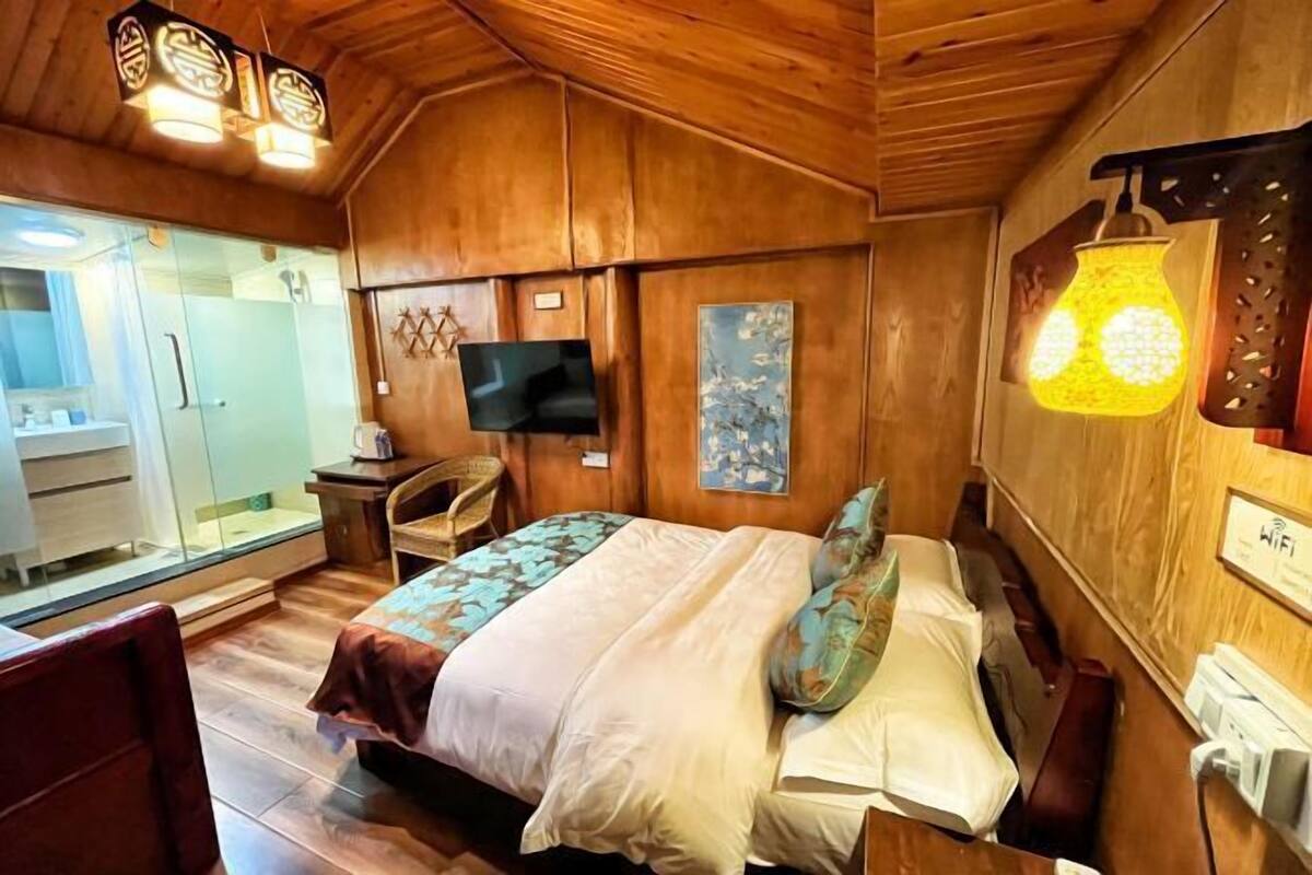 A wooden-themed bedroom with a bed, a TV, and a glass shower area.