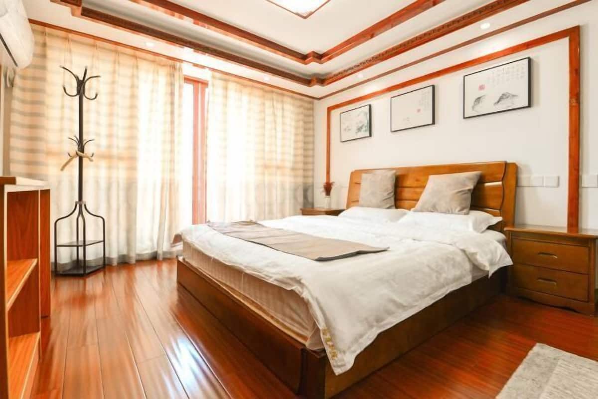 A bedroom with a wooden bed, a nightstand, a coat rack, and a window with curtains.