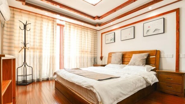 A bedroom with a wooden bed, a nightstand, a coat rack, and a window with curtains. - Yunsu Hotel (Kunshan)