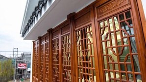 A traditional wooden gate with intricate carvings, leading to a building with a white facade and a sign above. - Yunsu Hotel (Kunshan)
