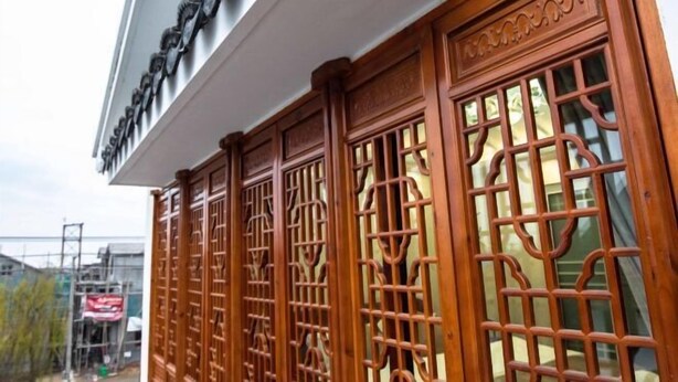 A traditional wooden gate with intricate carvings, leading to a building with a white facade and a sign above.