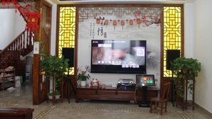A living room with a flat-screen TV mounted on a wall with decorative panels, a wooden entertainment unit below, and a staircase with red decorations. - Yunsu Hotel (Kunshan)