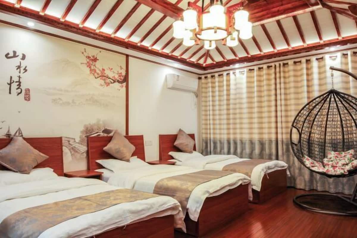A hotel room with two beds, a hanging chair, a wooden ceiling, and a wall with calligraphy.