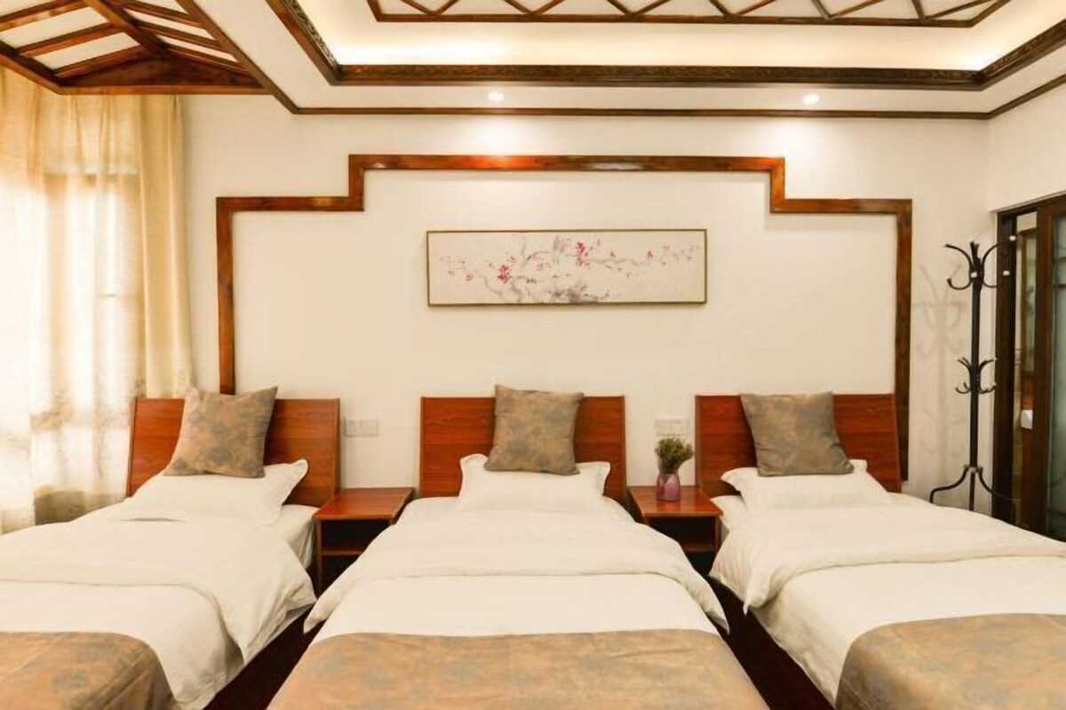 A hotel room with three beds, wooden headboards, a wall-mounted artwork, and a window with curtains.