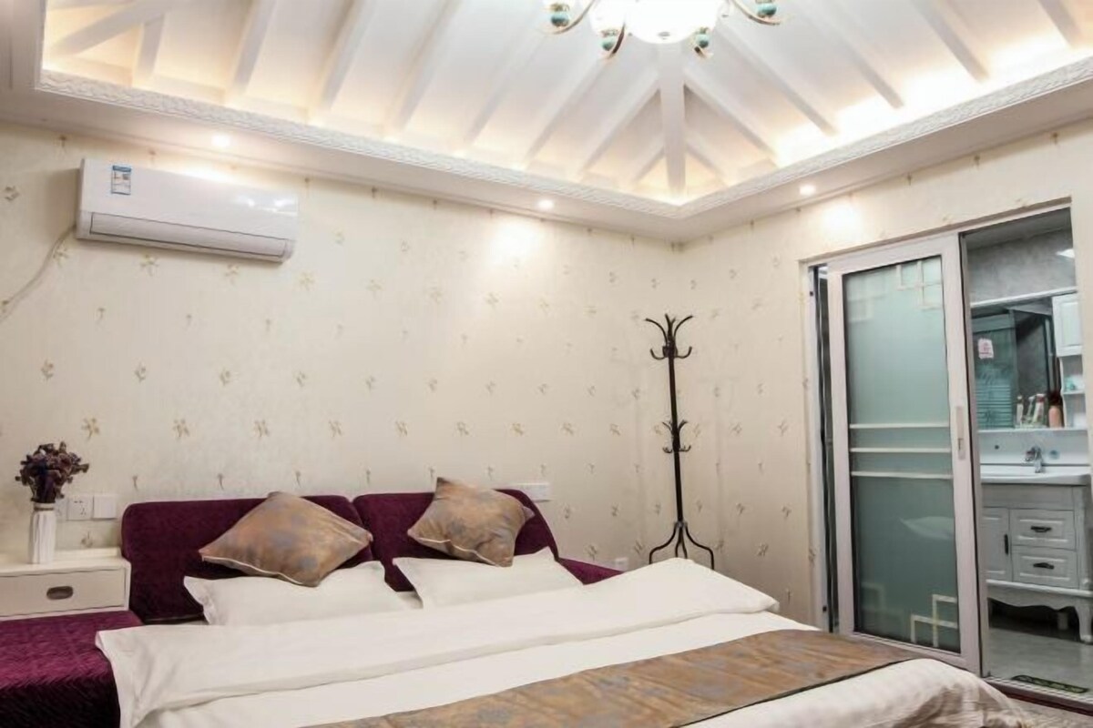 A bedroom with a bed, a nightstand, a floor lamp, and a sliding glass door leading to a bathroom.