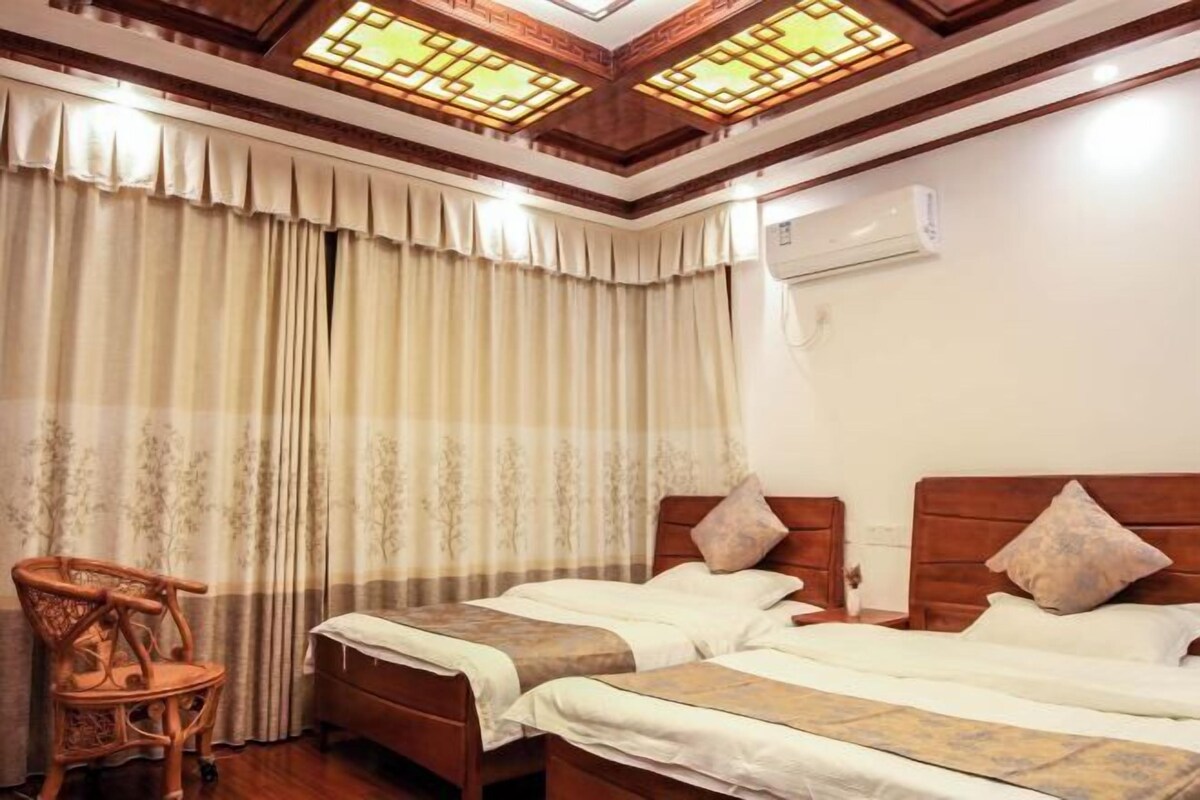 A hotel room with two beds, a wooden chair, a window with curtains, and a ceiling light fixture.