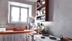 A kitchen with a white stove, a sink, and a window. - Calderimi,Traditional house in the center of Santorini. (FIRA)