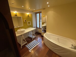 Une salle de bain moderne dotée d’une grande baignoire, de deux lavabos et d’une fenêtre laissant entrer la lumière naturelle.