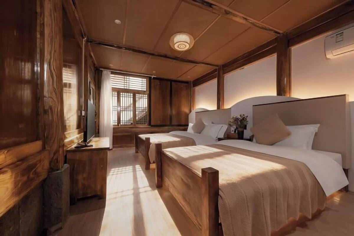 Une pièce aux murs en bois, avec un grand lit, une table de chevet et une fenêtre équipée de stores.