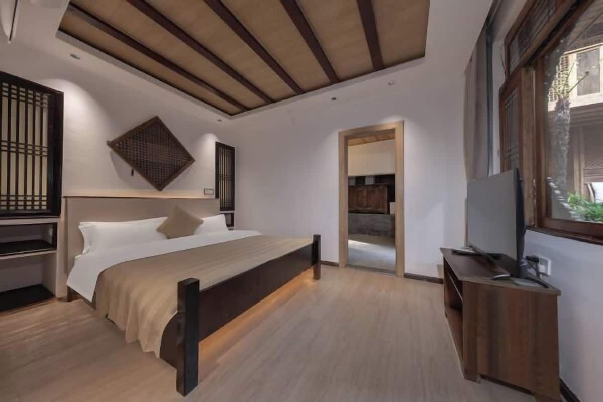 Une chambre à coucher comprenant un lit, une tête de lit en bois, une table de chevet, un meuble pour la télévision et une fenêtre donnant sur un beau paysage.
