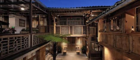 A traditional courtyard with wooden architecture, a central seating area, and a night sky.