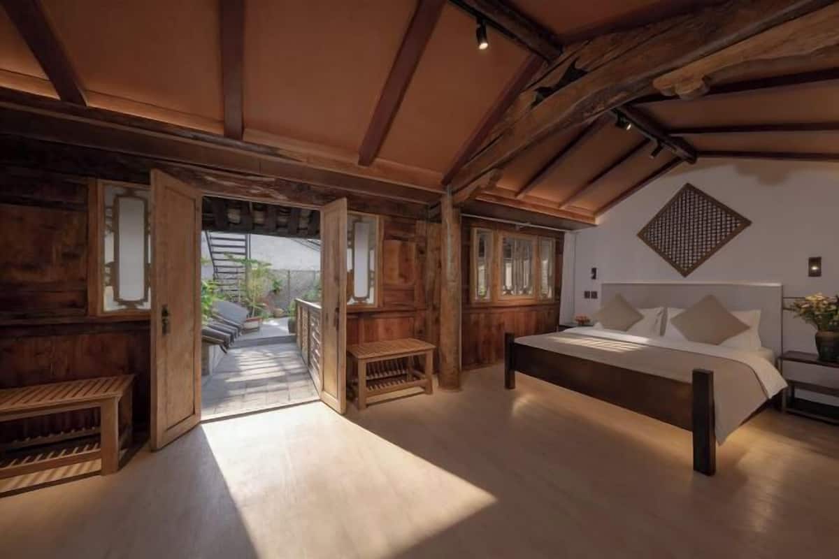 Une chambre avec un plafond en bois, un lit, une table de chevet et une fenêtre.