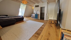 A spacious living room with a large window, a sofa, a wooden coffee table, and a television. - Vacation apartment Friesenwind (Rantrum)