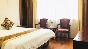 Una habitación de hotel con una cama grande, dos sillones de cuero, una mesita con una planta y un piano.