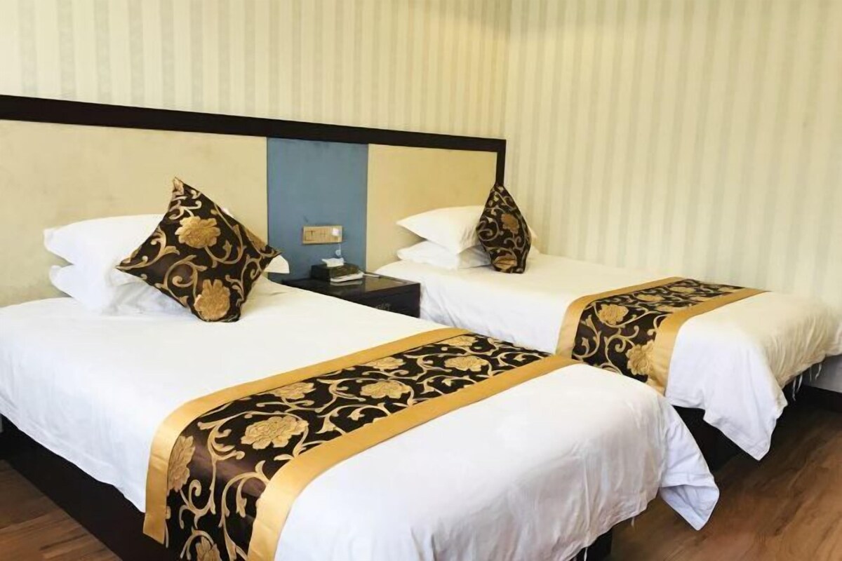 Two twin beds with white bedding and gold patterns, a nightstand with a lamp, and a striped wall.