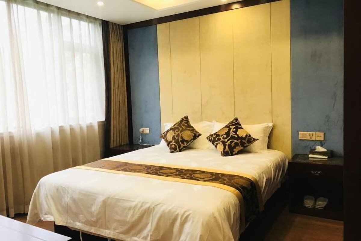 A hotel room with a large bed, a bedside table, and a window with curtains.