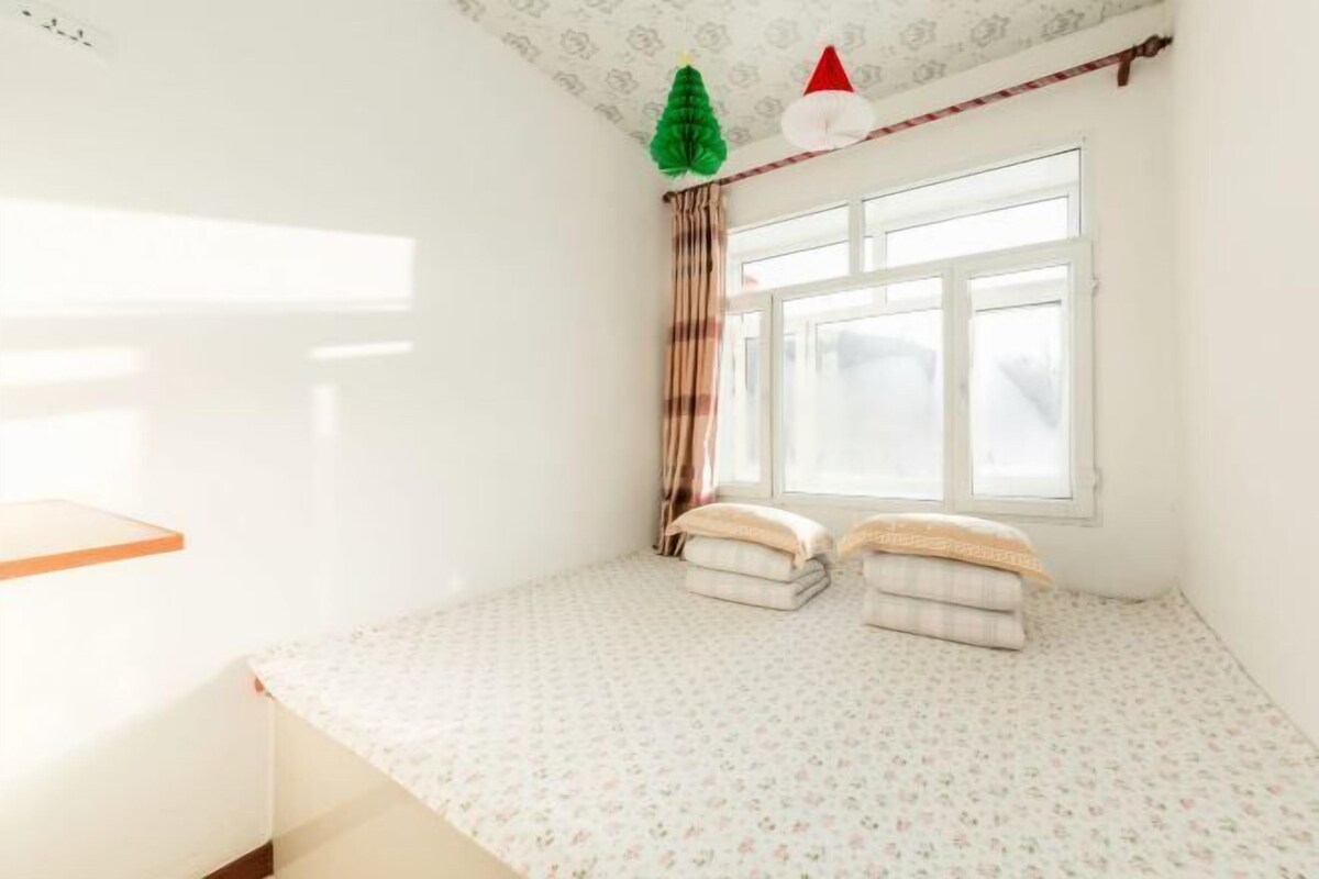 A bedroom with a bed, a window with curtains, and a small shelf.