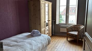 Een slaapkamer met een bed, een houten kledingkast, een stoel en een raam met uitzicht op gebouwen.