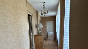 Un pasillo con piso de madera, un candelabro y una puerta que da a un baño.