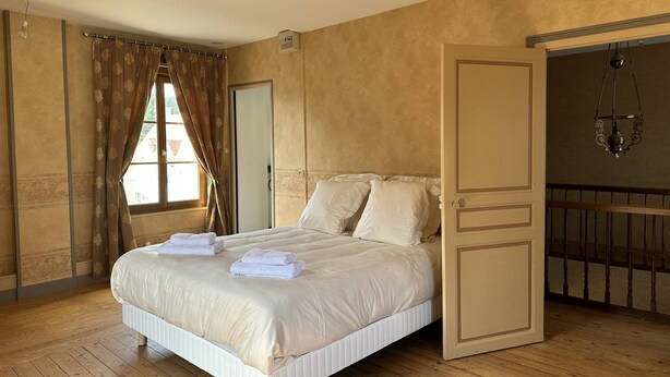 Un dormitorio con cama, ventana con cortinas, puerta y balcón con lámpara colgante.