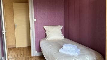 Ein Einzelbett mit weißer Matratze und Kissen, Holzboden und eine Tür zu einem anderen Raum.