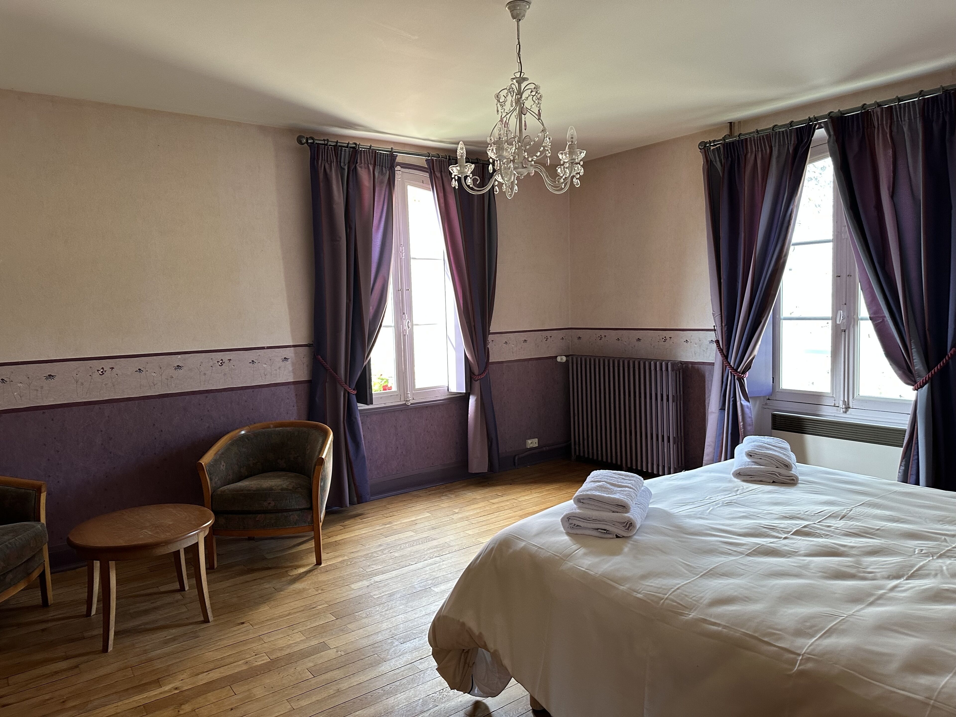 A hotel room with a bed, a chair, a small table, and a chandelier.