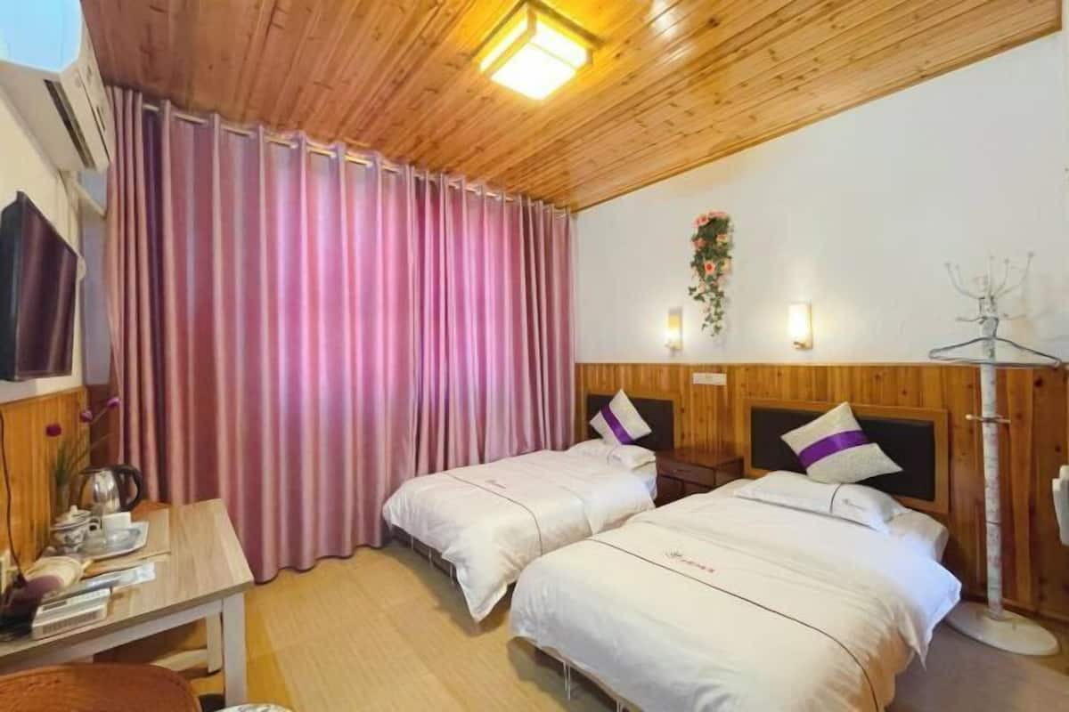 A room with two beds, a wooden ceiling, a table with a kettle, and a wall-mounted TV.