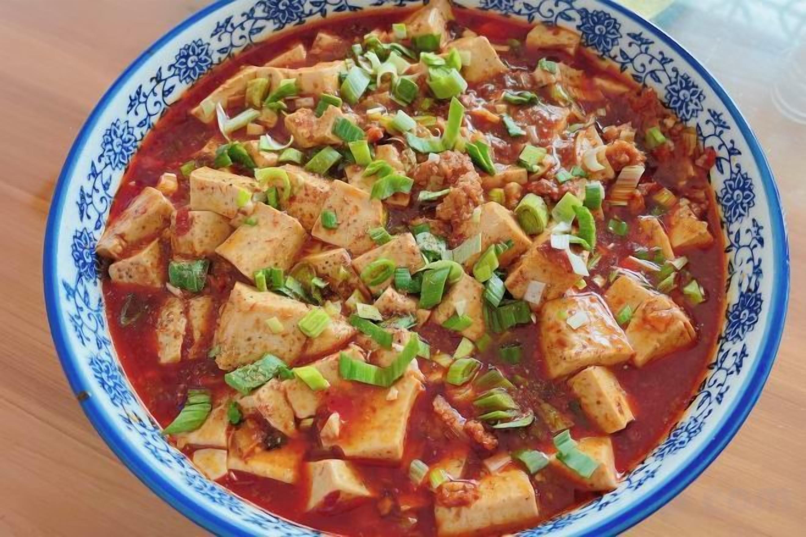 A bowl of food with tofu and green onions.